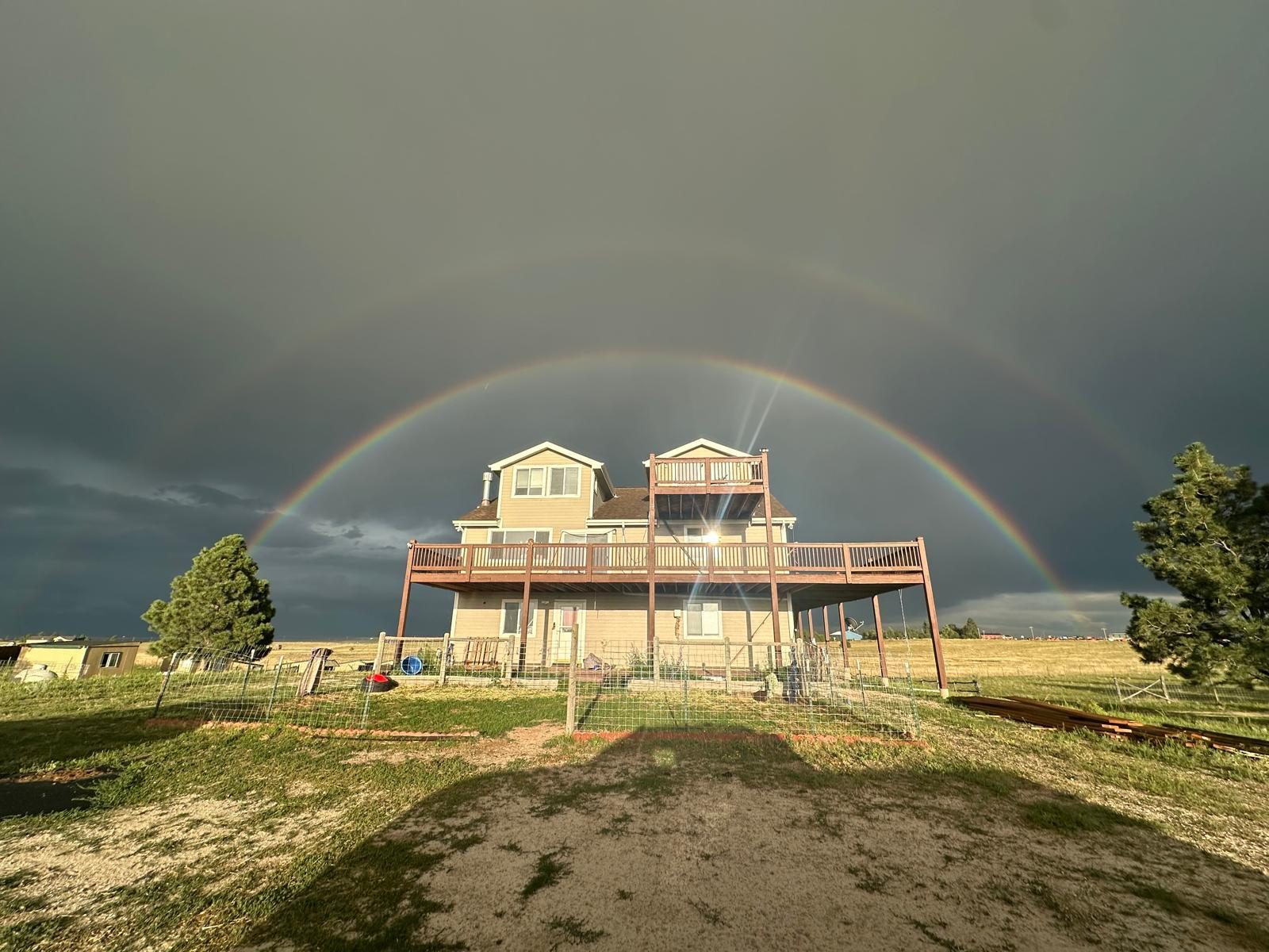 A full rainbow arching over the farmhouse and open pasture at the Truck Yeah Traders farm